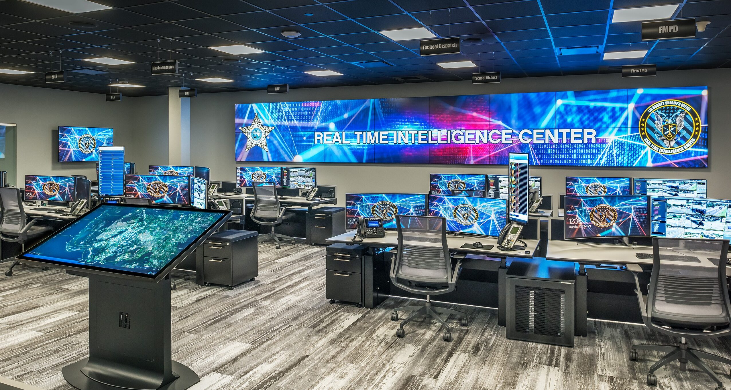 Curved ergonomic desks facing a large, lit multi-panel command center video wall