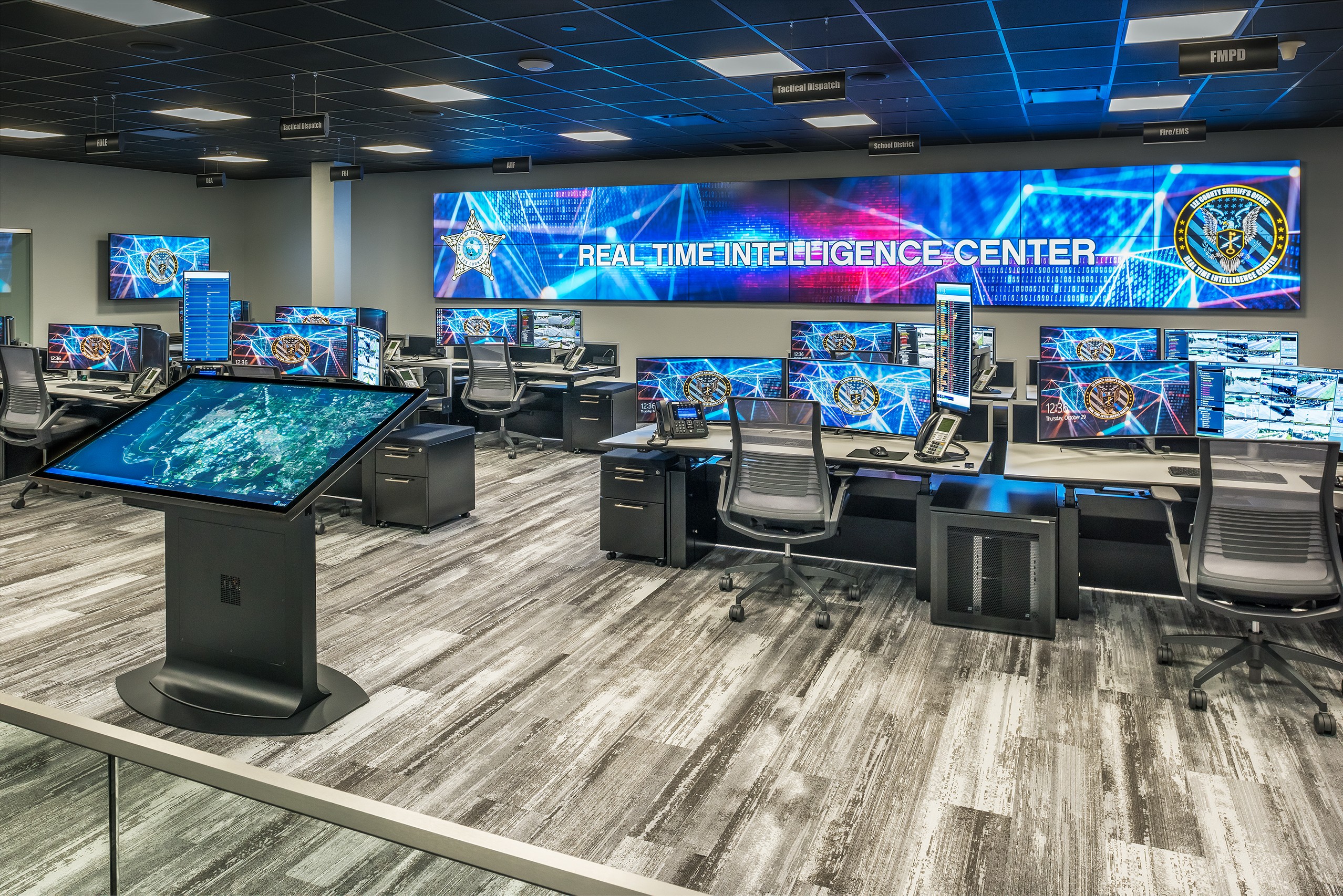 Curved ergonomic desks facing a large, lit multi-panel command center video wall