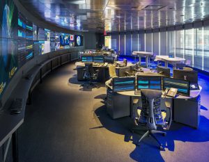 Darkly lit operations center with colorful accent lights, large video wall, and console furniture