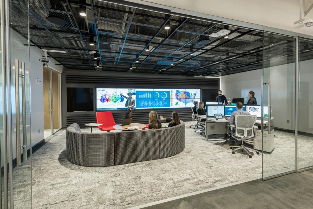 Image of a social media command center with large video wall, couch, and employees collaborating