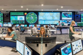People working in a Fleet Operations Center with video walls and consoles