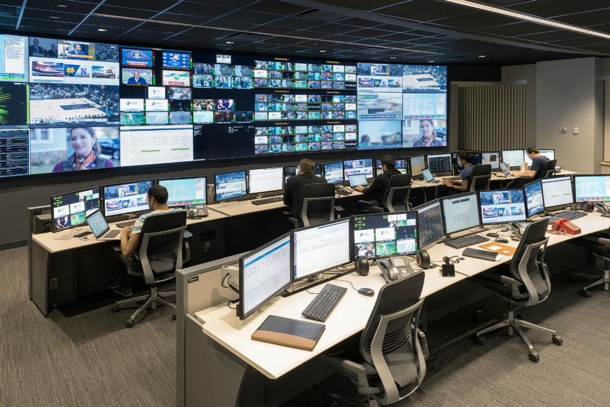 Five people working in an Command Center with video walls and consoles
