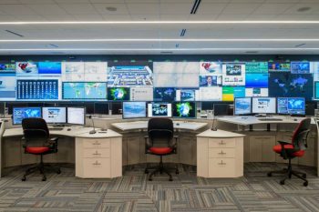 Command center video wall with workstations displaying global data and weather monitoring systems