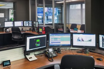 Modern operations center with curved multi-monitor workstations, glass-walled collaborative spaces