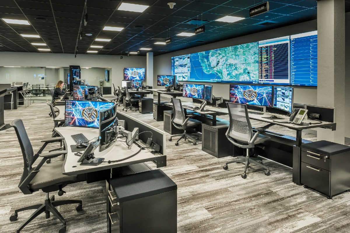 View of real time crime center with rows of console furniture and a large central video wall