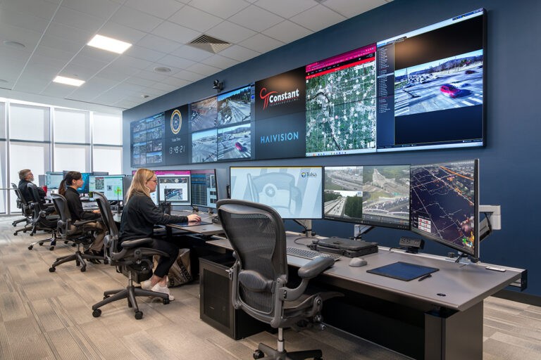 people working at desks in front of computers and a wall of large monitors